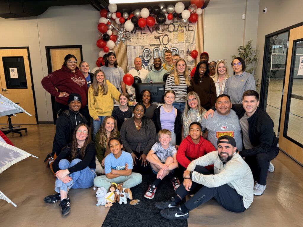 Group of students and staff posing for a photo in a festive space with red, white, and black balloons and a 'Welcome' backdrop behind them.