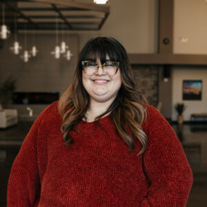 Smiling woman wearing patterned glasses and a red knit sweater indoors.